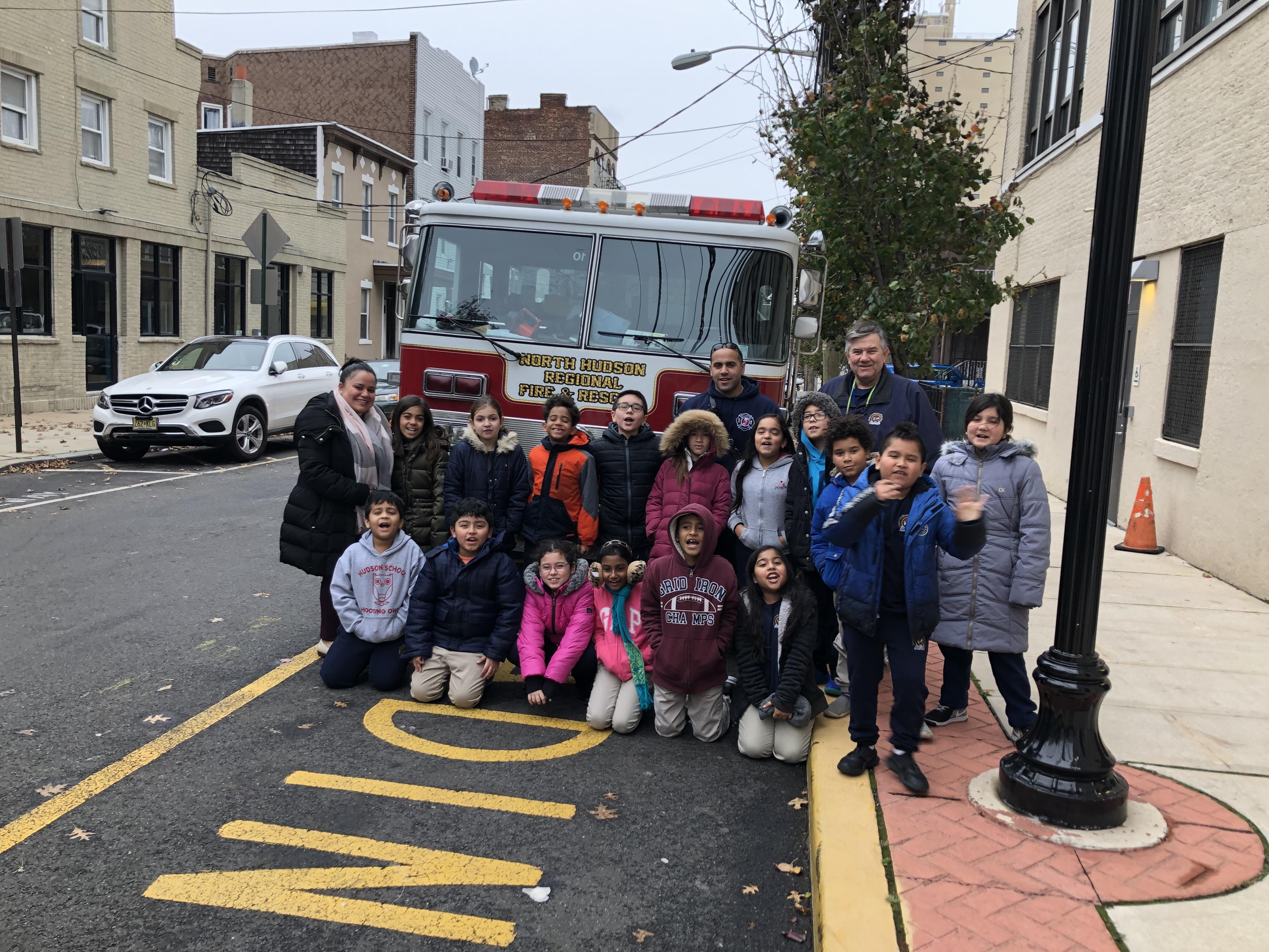 North Hudson Firefighter with a another class of students and their teacher in front of the fire engine in the front of the school